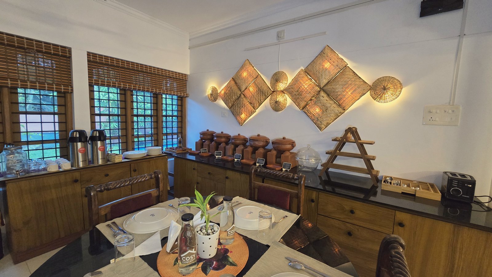 The dining room at Casa, a table laid for breakfast under woven lamps on the wall