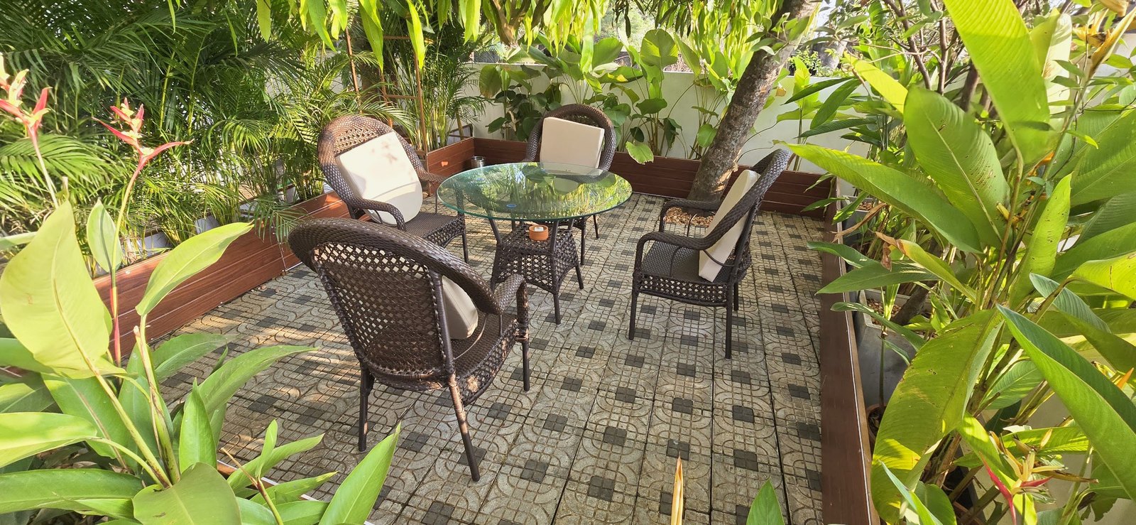 Open seating in the Casa garden, cane chairs around a table on patterned tiles under the trees