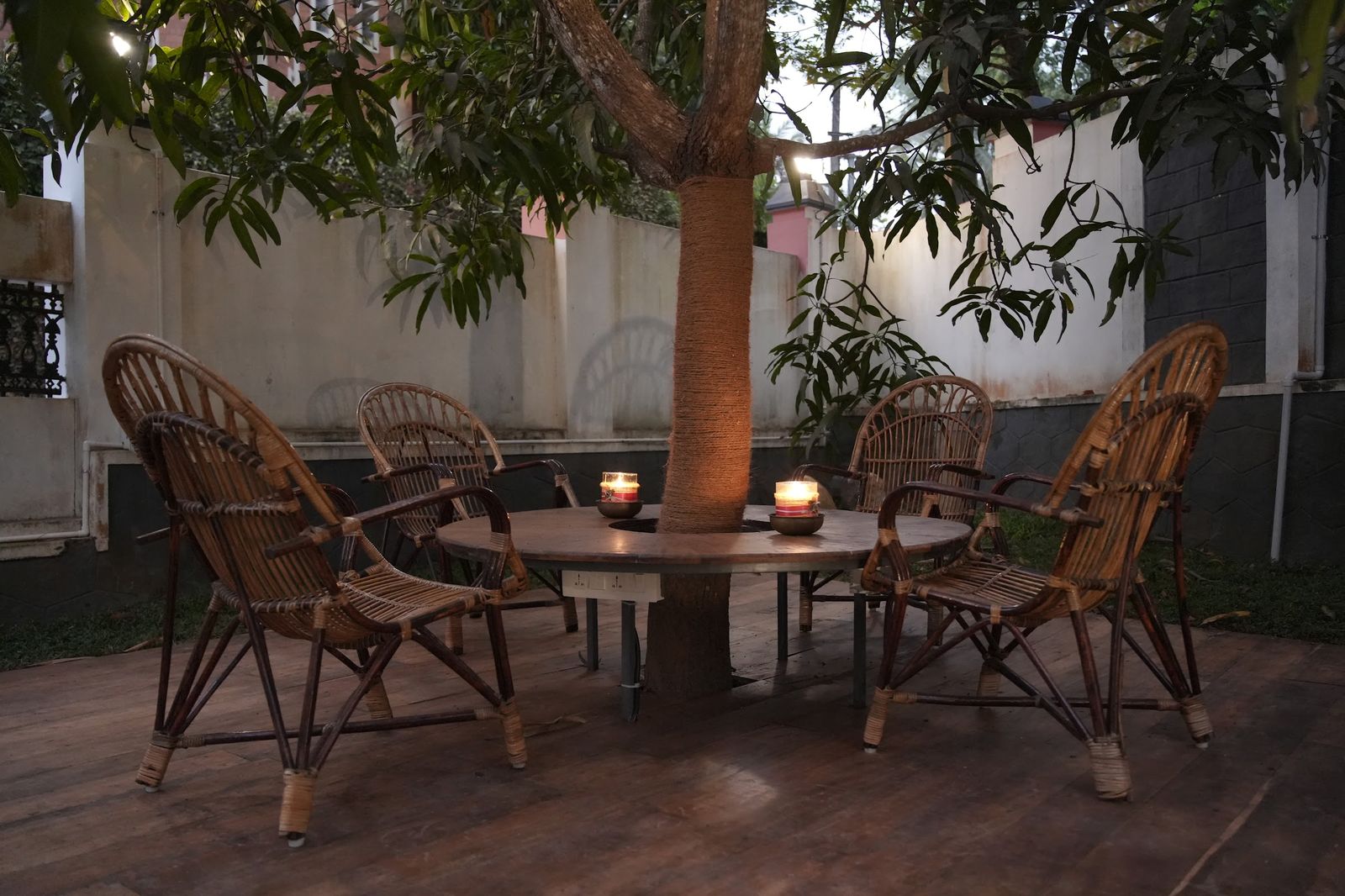 Cane chairs around a table under the mango tree at Casa, a candle lit at dusk